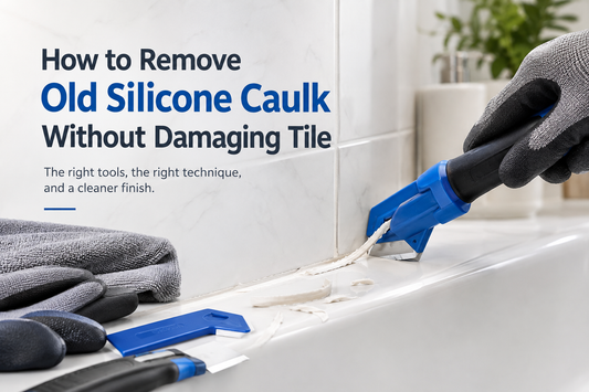 Gloved hand using a blue caulk removal tool to lift old silicone from the joint between white tile and a bathtub.